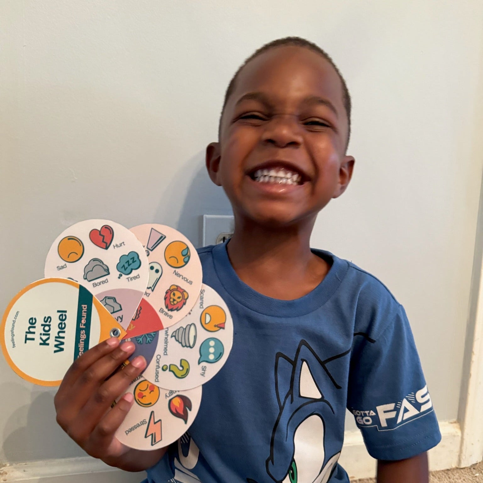 Child holding a colorful wheel with &#39;The Kids Wheel&#39; branding, wearing a blue t-shirt with a cartoon character.